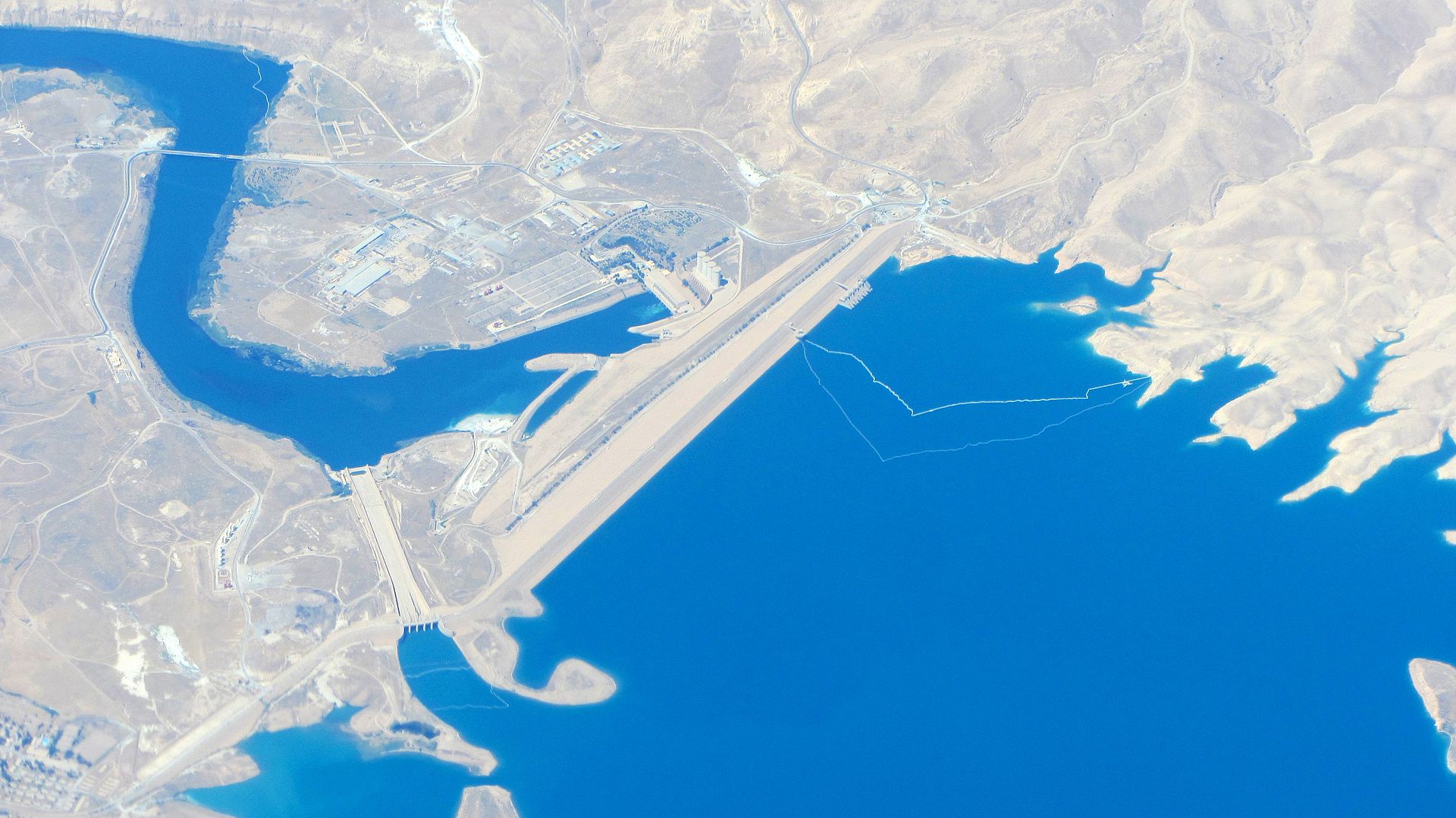 Aerial view of the Mosul Dam, showing the earth-fill embankment, the spillway, and the reservoir behind it.