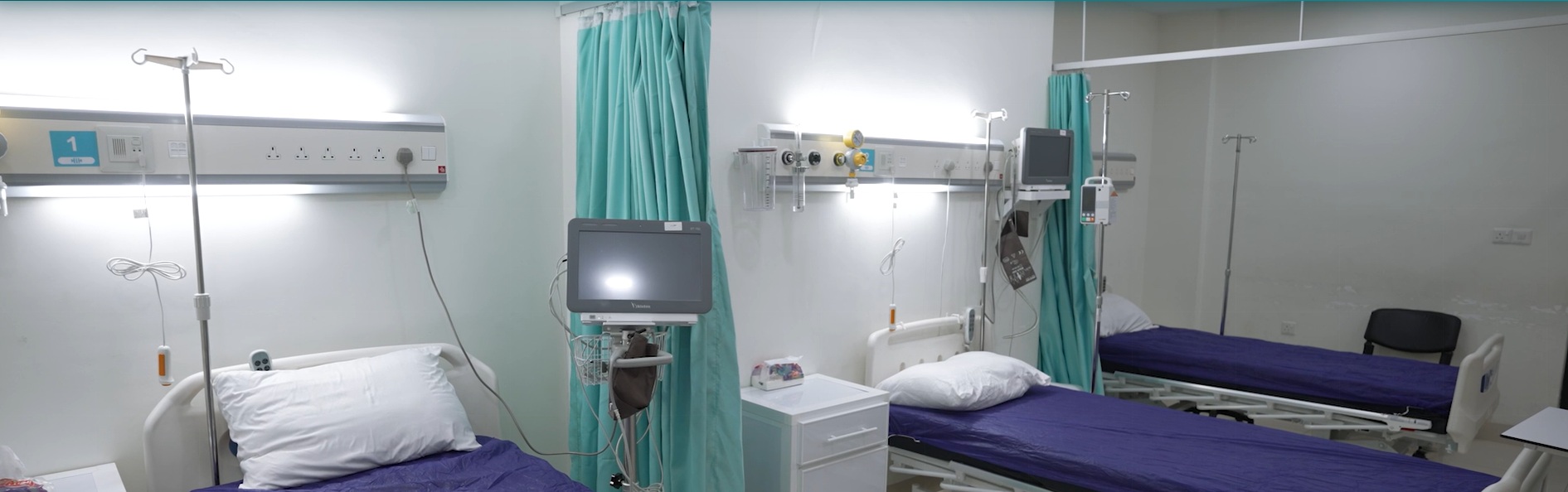 A modern equipped two-bed ward at Al-Hayat International Hospital, Mosul — fitted with vital-signs monitor, infusion equipment, piped oxygen and patient call-system.